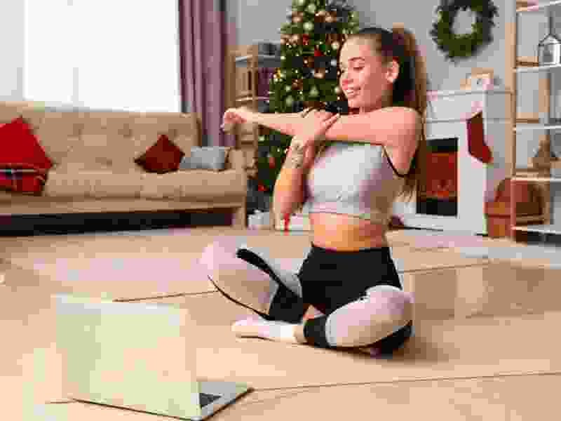 Woman doing an arm stretch at home in front of a laptop